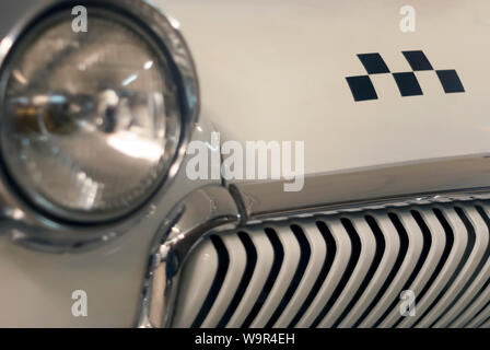 fragment of the front part of a vintage taxi car, focus on the checker emblem and radiator, headlight is in blur Stock Photo