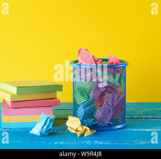 blue metal bucket filled with crumpled multi-colored white paper, yellow  background, business concept Stock Photo