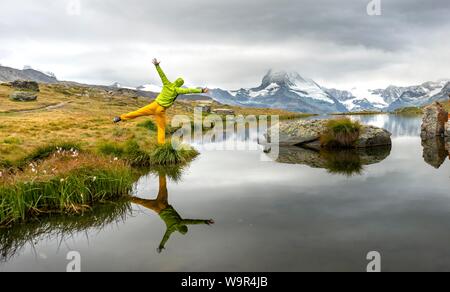 Hiker stretches his arms into the air, Lake Stellisee, Matterhorn at the back, cloudy, Wallis, Switzerland Stock Photo