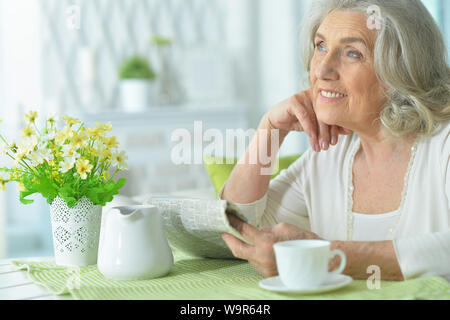 Portrait of senior woman reading newspaper and posing at home Stock Photo