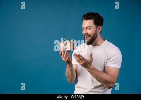 Image of a handsome young excited man posing isolated over blue wall background holding present gift box. Portrait of a handsome man. Stock Photo