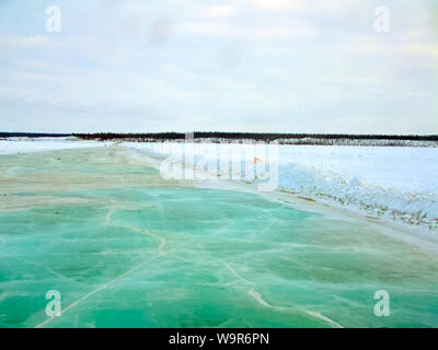 The frozen river thaws. Algae under the ice painted it in green Stock Photo