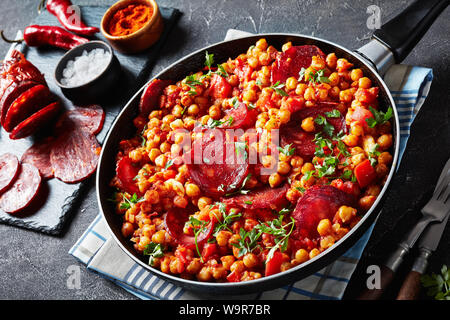 close-up of Garbanzos fritos, stewed Chickpeas with chorizo, ham, tomatoes and spices in a skillet on a concrete table with ingredients, spanish cuisi Stock Photo