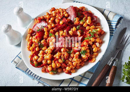 Garbanzos fritos, hot Chickpea stew with sliced chorizo, ham, tomatoes and spices on a white plate on a white concrete table, spanish cuisine, view fr Stock Photo