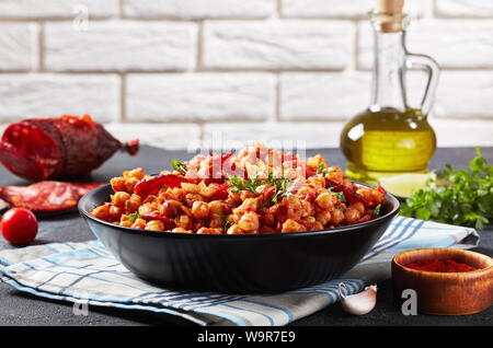 close-up of Garbanzos fritos, hot Chickpea stew with chorizo, tomatoes and spices in a black bowl on a concrete table with ingredients at the backgrou Stock Photo