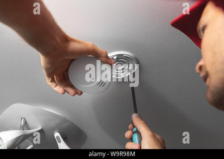 handyman installing smoke detector on ceiling at home Stock Photo