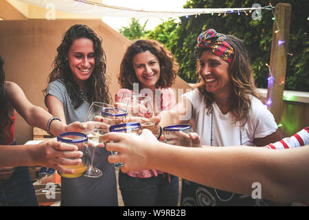 Group of happy friends cheering with glasses at dinner outdoor in terrace. Teenager and mothers having fun while drinking and eating. Focus on glasses Stock Photo