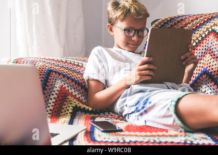 Beautiful smiling teen reading new trend stories online on tablet. Technology addicted young boy watching social video at home. Teenager communicate w Stock Photo