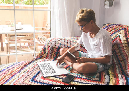 Beautiful blonde teen reading new trend stories online on laptop. Technology addicted young boy watching social video at home. Teenager communicate wi Stock Photo