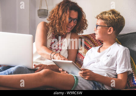 Beautiful teen reading new trend stories online on tablet with mum. Technology addicted young boy watching social video at home with his mother. Child Stock Photo