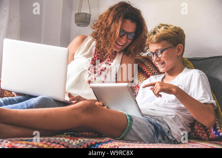 Beautiful teen reading new trend stories online on tablet with mum. Technology addicted young boy watching social video at home with his mother. Child Stock Photo