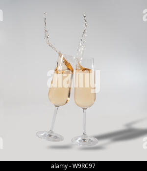 Two glasses of Champagne chink together, drink splashes out Stock Photo