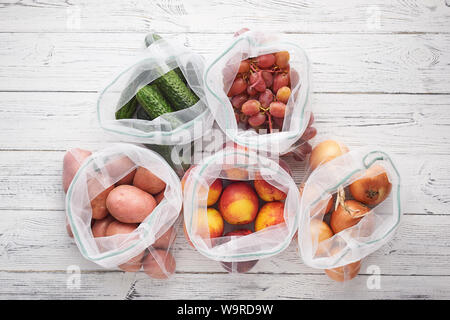 Fruits and vegetables in reusable eco bags at white wooden background. Recycled bags instead of plastic bags. Plastic free. Top view flat lay Stock Photo