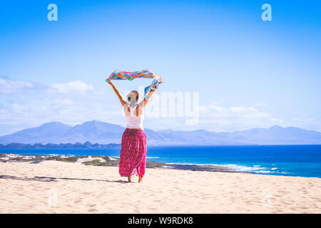 Beautiful young girl with flies scarf in his hands over white sand dunes in Fuerteventura. Colorful exotic vacation postcard. Blue ocean and sky in ba