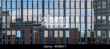 Cityscape reflected on the windows of a modern building near the international airport of Vienna. Views of various buildings and blue sky with clouds Stock Photo