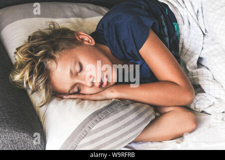 Young boy sleeping with hands on the pillow. Beautiful child sleeps alone in the bed dreaming about vacation. Teen is resting at home pleasantly relax