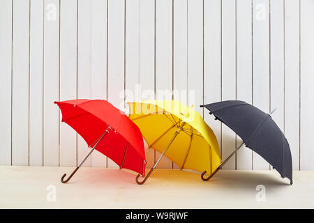 Three umbrellas on floor near white wooden background with space for design Stock Photo