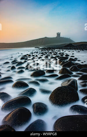 An early morning shot of Dunstanburgh castle along the black boulder beach Stock Photo