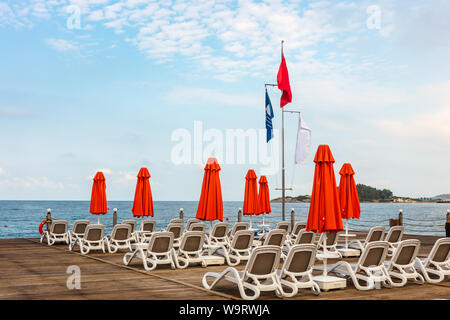 Rows of white sun beds with red parasols on a wooden pier in the sea. Stock Photo