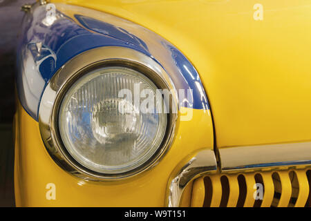 detail of the front part of a blue-yellow vintage car, headlight and radiator fragment Stock Photo