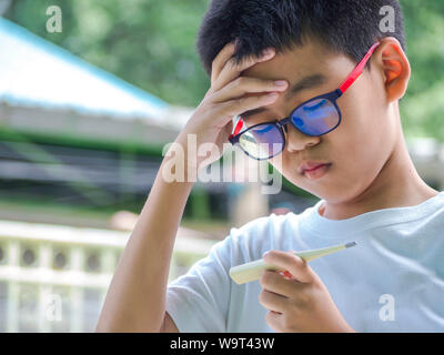 Asia boy measuring temperature of himself ill. Sick child with high fever and holding thermometer. Stock Photo