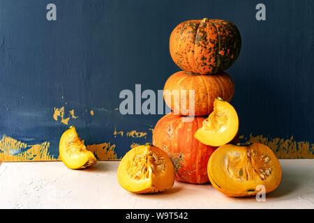 Large ripe pumpkins and cut pieces on a white concrete table against a painted blue wall Stock Photo