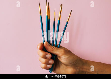 hand holds paint brushes on the pink background Stock Photo