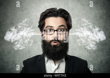bearded surprised man, blowing steam coming out of ears, over gray background, negative human emotions, facial expression, feelings Stock Photo