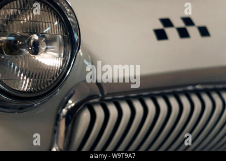 monochrome fragment of the front part of a vintage taxi car, focus on the headlight, checker emblem and radiator in blur Stock Photo