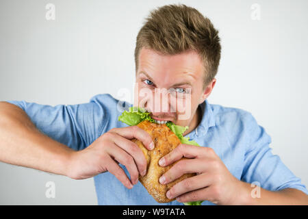young handsome hungry man biting fresh sandwich with salad leaf on isolated white background. Stock Photo