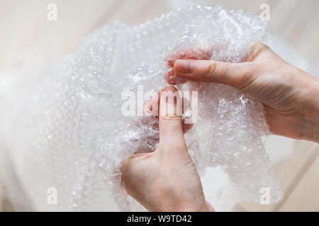 Female hands popping the bubbles in bubble wrap. Selective focus, close up. Stock Photo