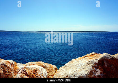 Seascape view with big rocks in front of blue sea surface on which the sun rays are reflected all the way to the horizon line Stock Photo