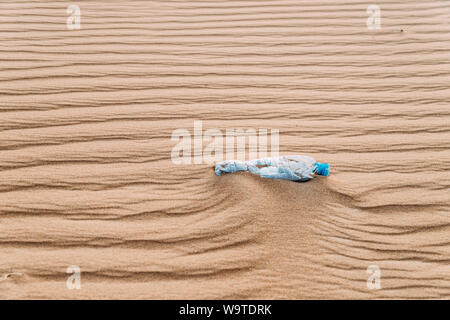 A used plastic bottle of water sitting in a sand dune desert with patterns. Stock Photo