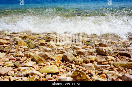 Dynamic tidal white wave splashing on the pebbles sea coast and beach with pebbles on a sunny day Stock Photo