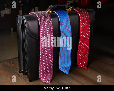 Men's ties are thrown over the men's briefcase in the accessories store. Stylish accessories. Colorful fabrics. European fashion Stock Photo