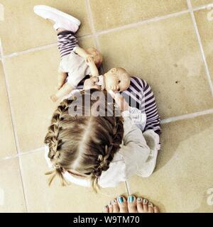 Overhead view of a woman's feet next to a girl sitting on the floor playing with dolls Stock Photo