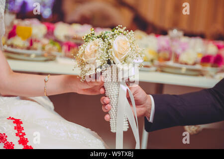 Hands folded behind their back, hold a beautiful white little wedding bouquet of roses . They held the white flower bouquet in their hands Stock Photo