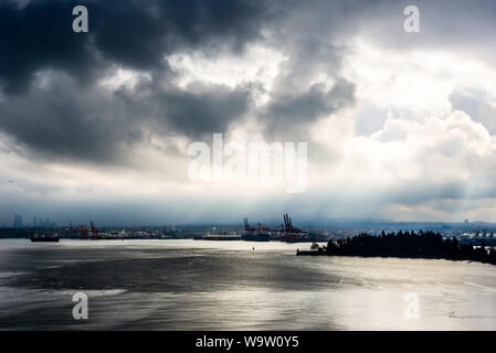 Sun breaking through from behind dark clouds in high contrast over water in Vancouver, British Columbia, Canada. Stock Photo