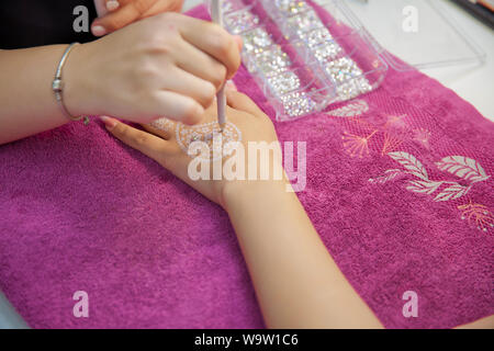 Draws henna into his hands . the master draws in the form of a buta feather on his hand with white gel . street artist draws henna patterns on his han Stock Photo