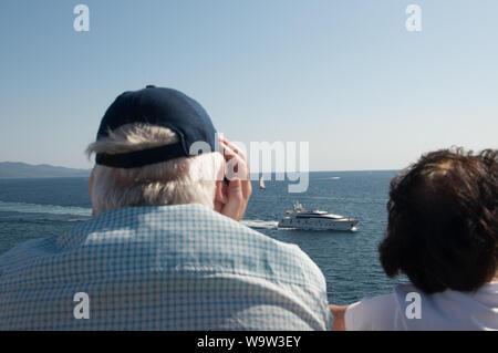 Ajaccio, corsica, 2019-08-04, Super yacht at sea with visable long wash behind, male and female spectators watching it pass bye Stock Photo