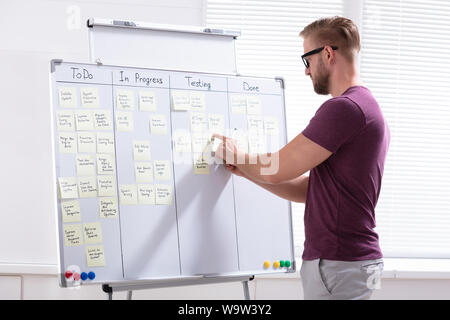 Side View Of Young Businessman Writing On Sticky Notes Attached To White Board In Office Stock Photo
