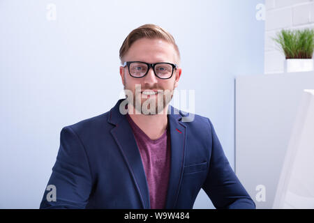 Close-up Of A Bearded Businessman Looking At Camera Sitting Near Computer Monitor In Office Stock Photo