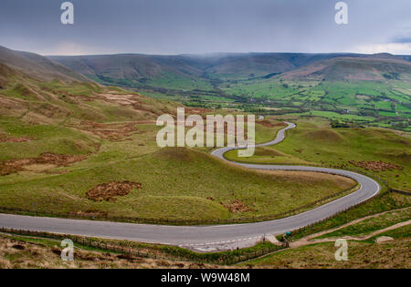 A narrow country lane winds across moorland at Mam Tor in the Derbyshire Peak District, with Edale and the Kinder Scout hills behind. Stock Photo