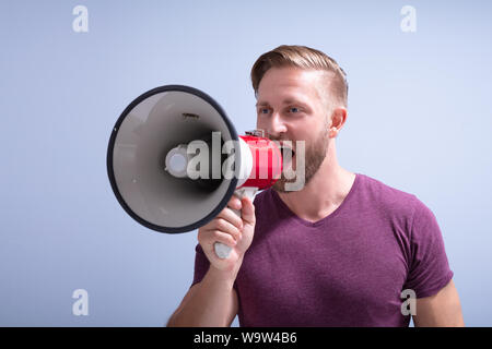 Close-up Of A Beard Man Shouting Through A Megaphone Against Gray Background Stock Photo