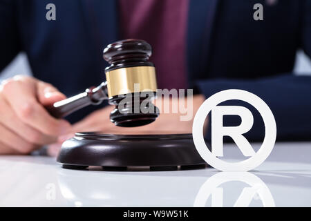 A Person's Hand Hitting The Gavel On Sounding Block Near Trademark Icon Over Desk Stock Photo