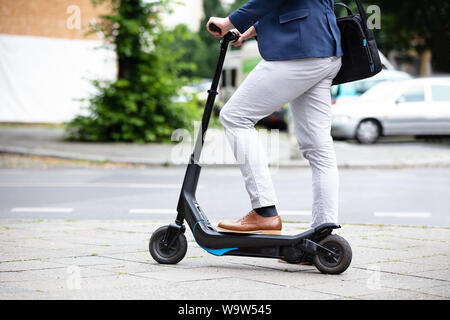 Low Section Of A Businessman Standing On Electric Scooter At Street Stock Photo