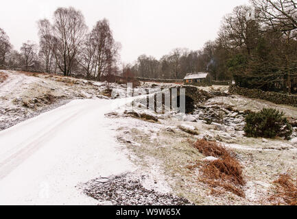 Winter snow lies on the picturesque stone arch bridge and traditional barn at Ashness in the woodland above Derwent Water in the English Lake District Stock Photo