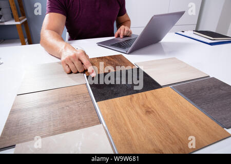 Male Interior Designer Choosing Color Of Tiles With Laptop Working At Workplace Stock Photo