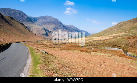 A narrow country lane winds through the valley floor of Honister Pass under the mountains of England's Lake District. Stock Photo