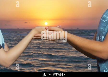 They caught the sun in their families. Sunrise .Held hands in the background of the sun and the sky. Hands of holding each other on lake and sun .Two Stock Photo